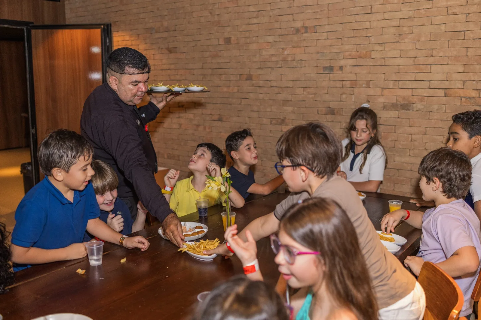 Garçom servindo lanches a crianças sentadas à mesa no espaço de festas